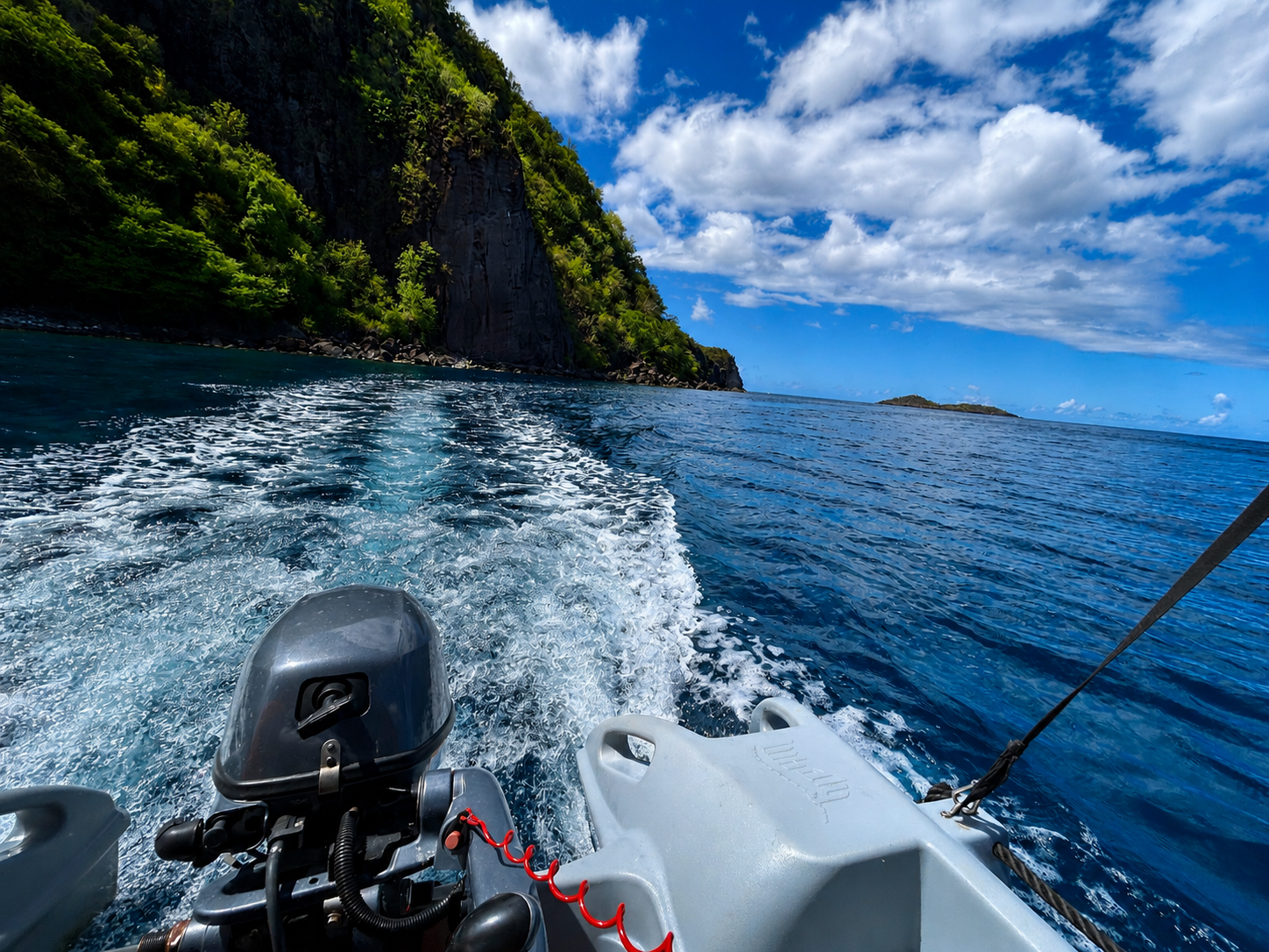 Vue depuis un bateau sans permis à Pointe-Noire, sur la côte sous-le-vent en Guadeloupe, avec falaises tropicales, mer bleue et paysage proche de la Réserve Cousteau au fond.